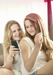 Immagine di due giovani donne. Una tiene un cellulare e l’altra si mette lo smalto sulle unghie. La foto mostra che i cambiamenti che si verificano nel corpo sono normali e a volte potete parlarne con amici e genitori.